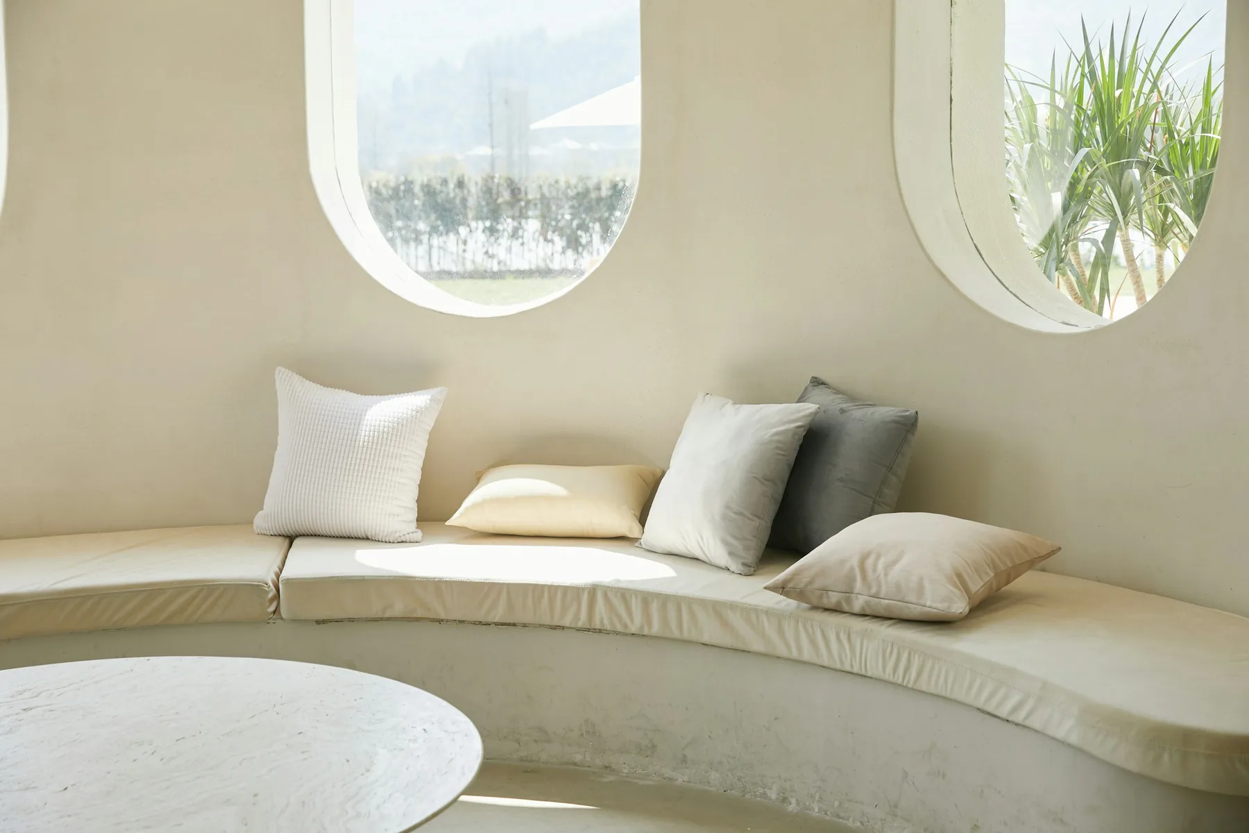Reference photograph of a curved cream window seat with neutral cushions beneath two arched windows
