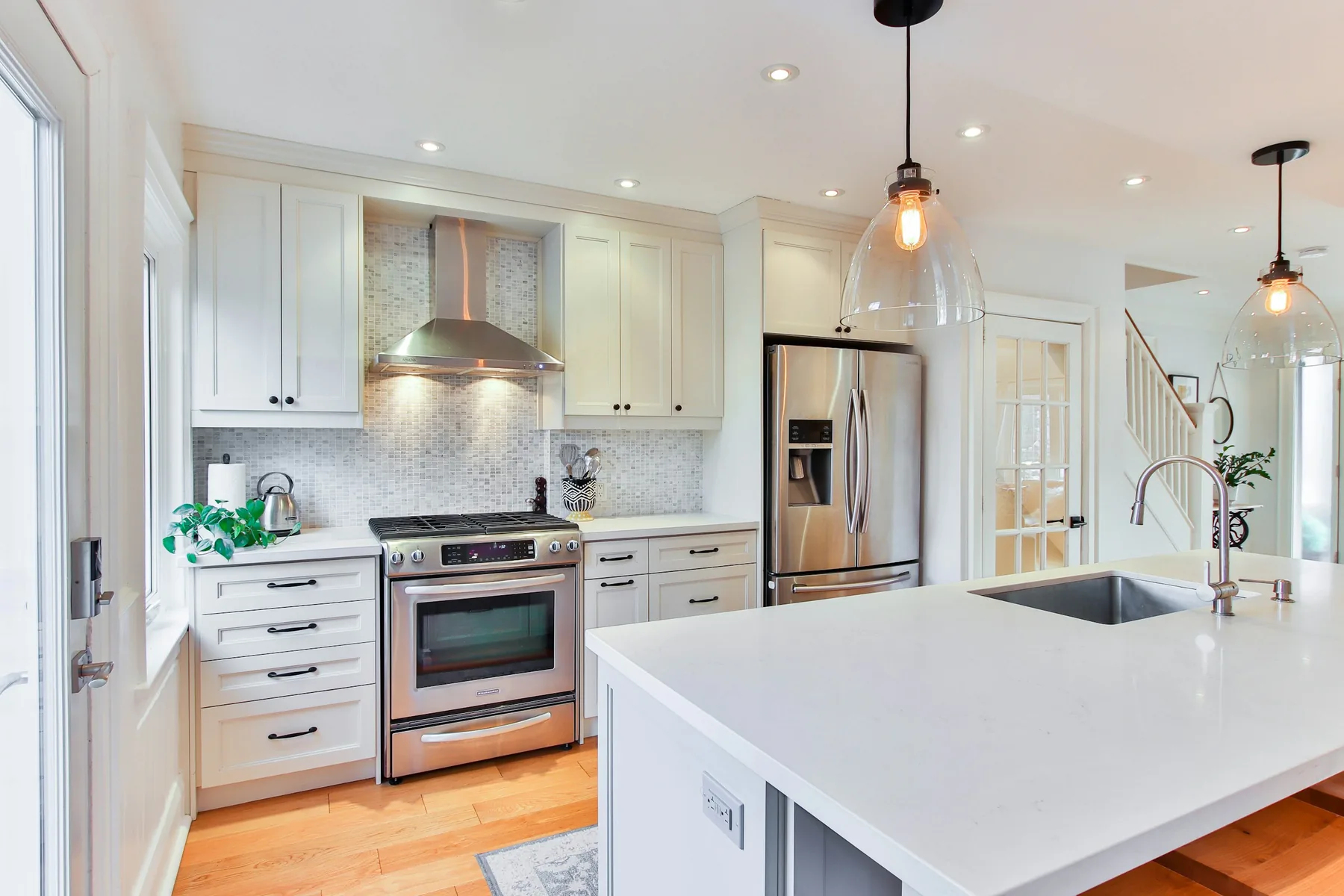 Bright white kitchen with shaker cabinets, a stainless steel range and refrigerator, glass pendant lights, and a white island